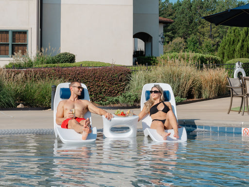 Two people sitting in TenJam Laylo Lounger chairs by a pool with a table between them.