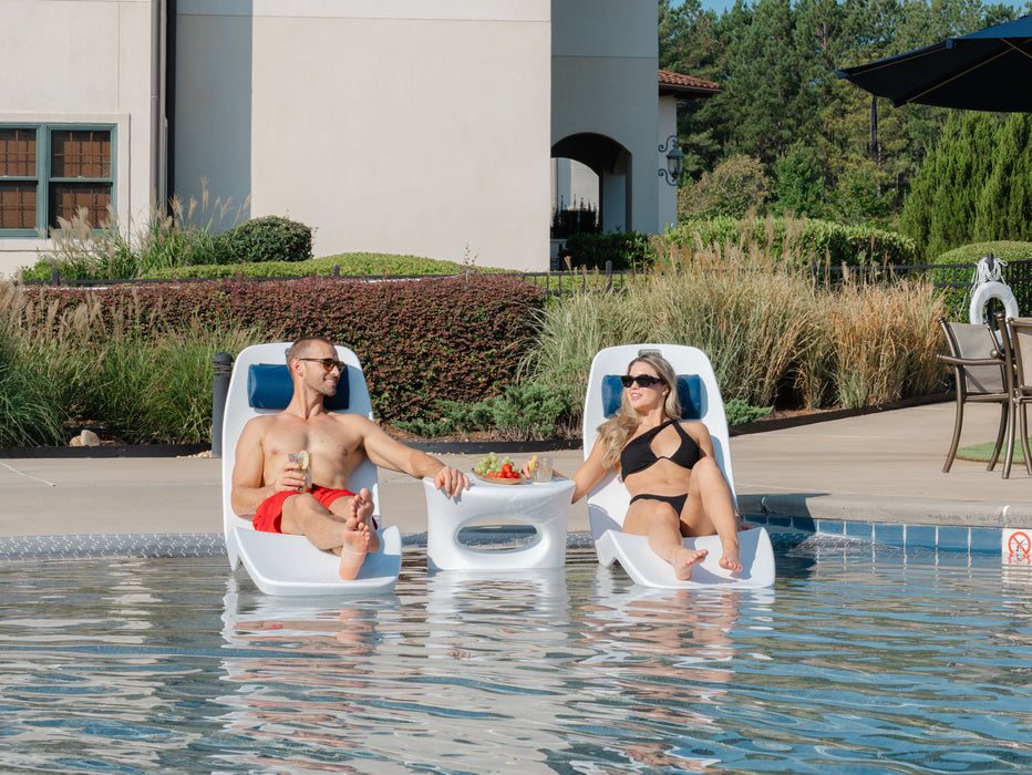 Two people sitting in TenJam Laylo Lounger chairs by a pool with a table between them.